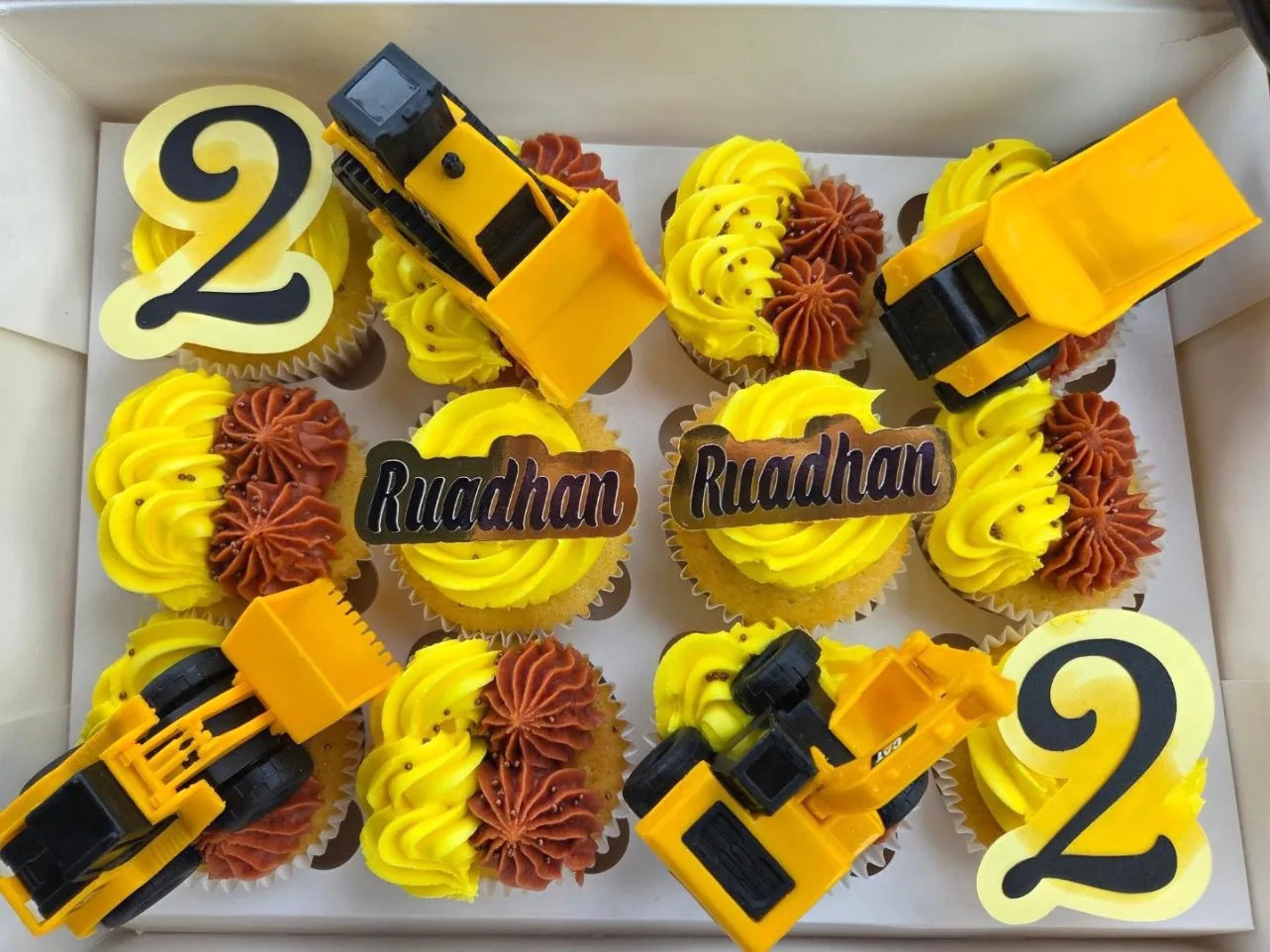 Box of yellow and chocolate cupcakes with toy diggers, number 2 toppers and Ruadhan name toppers