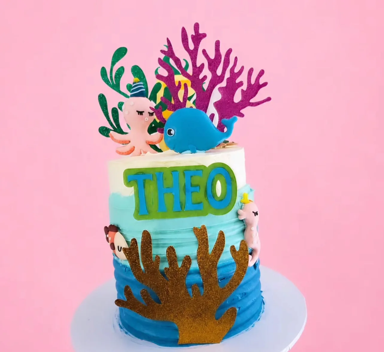 Ocean-themed cake in blue buttercream with coral, a whale, an octopus and a Theo name topper