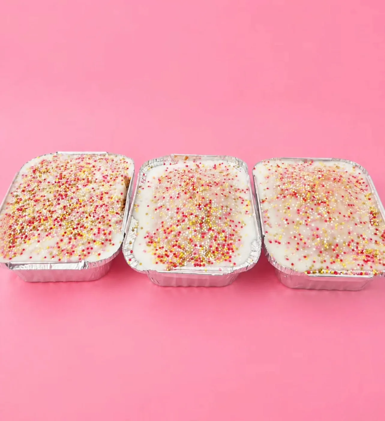 Three trays of iced traybake covered in colourful sprinkles